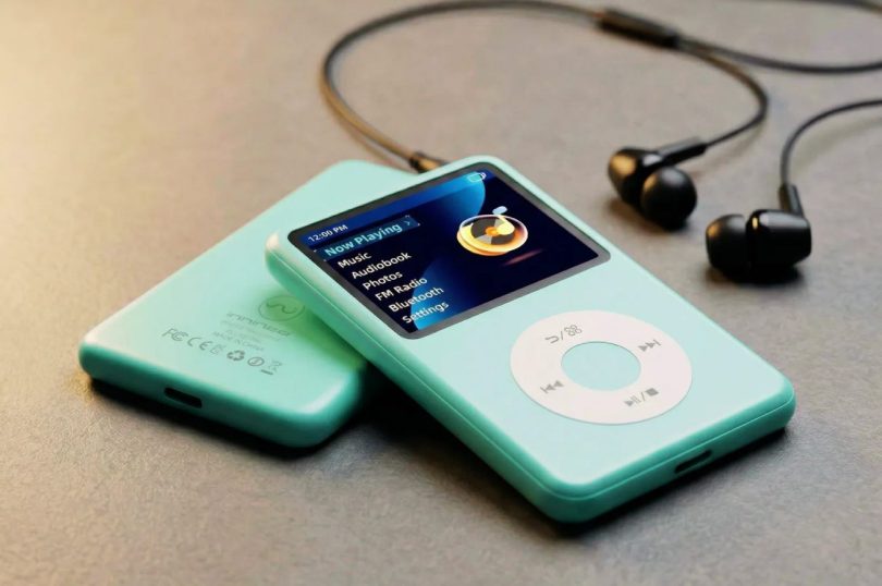 Lecteur MP3 nomade Innioasis Y1 128 Go en finition vert d'eau menthe avec écran couleur 1.8 pouces affichant l'interface Now Playing avec menus Music Audiobook Photos FM Radio Bluetooth Settings, molette tactile circulaire blanche signature inspirée iPod Classic, vue de trois-quarts avec un second exemplaire vu de dos en arrière-plan et écouteurs filaires noirs sur surface gris doré