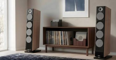 Paire d'enceintes colonnes Jamo Concert Legacy en finition Heritage noyer encadrant un meuble bas en bois clair contenant une platine vinyle et une collection de disques, dans un salon contemporain avec parquet clair, tapis sombre et tableau abstrait, configuration hi-fi audiophile scandinave