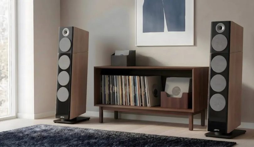Paire d'enceintes colonnes Jamo Concert Legacy en finition Heritage noyer encadrant un meuble bas en bois clair contenant une platine vinyle et une collection de disques, dans un salon contemporain avec parquet clair, tapis sombre et tableau abstrait, configuration hi-fi audiophile scandinave