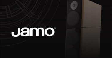 Visuel officiel du retour de la marque danoise Jamo en 2026 sous Cinemaster et Rayleigh Lab, logo Jamo blanc avec marque déposée à gauche sur fond noir et enceinte hi-fi deux voies en finition bois clair avec tweeter dôme et woofer à grille à droite, motif technique de tracé acoustique en filigrane suggérant l'ingénierie scandinave premium