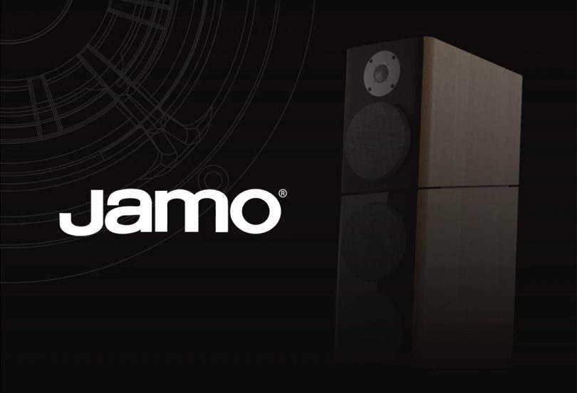Visuel officiel du retour de la marque danoise Jamo en 2026 sous Cinemaster et Rayleigh Lab, logo Jamo blanc avec marque déposée à gauche sur fond noir et enceinte hi-fi deux voies en finition bois clair avec tweeter dôme et woofer à grille à droite, motif technique de tracé acoustique en filigrane suggérant l'ingénierie scandinave premium