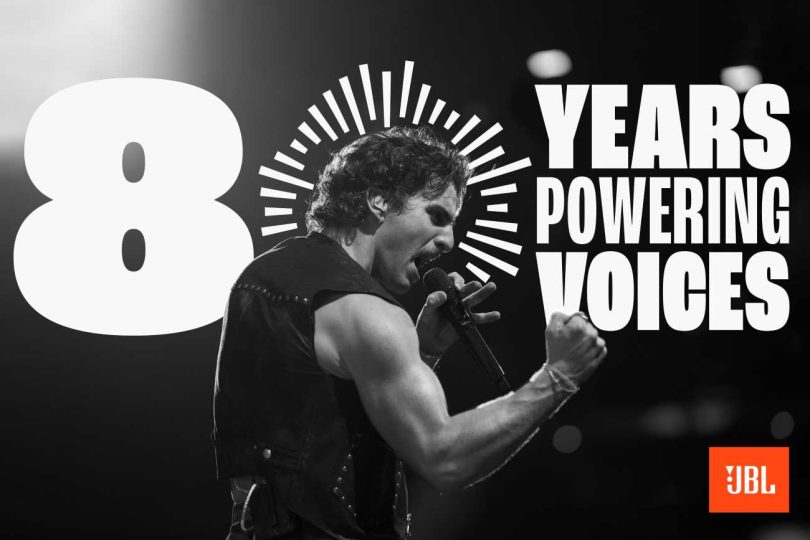 Visuel officiel de la campagne 80 ans de JBL en noir et blanc avec l'ambassadeur Benson Boone en performance scénique chantant dans un micro, signature 80 YEARS POWERING VOICES et logo JBL orange