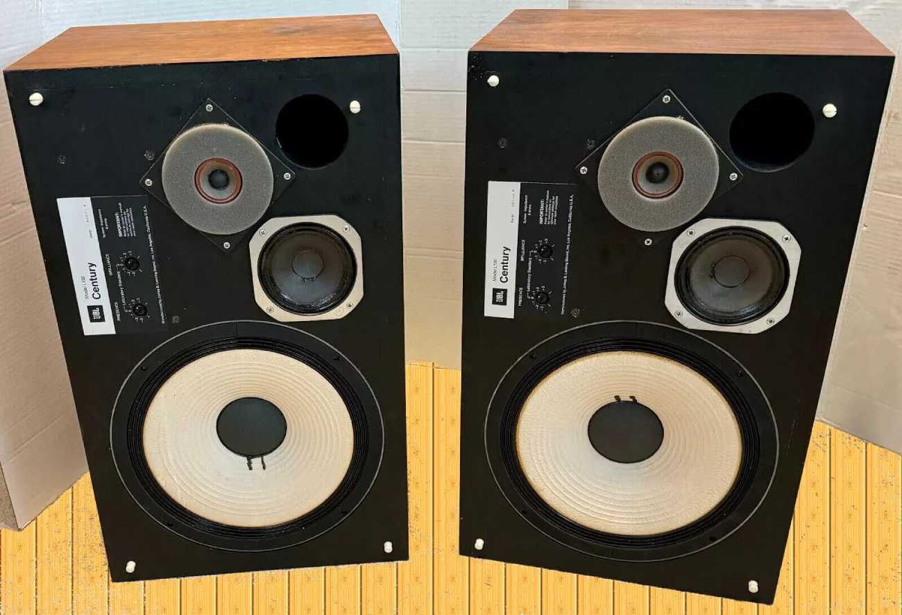Paire d'enceintes JBL L100 Century des années 1970 sans grille frontale, dévoilant le woofer 12 pouces à cône blanc, le médium 5 pouces et le tweeter dôme dans son baffle en losange, avec potentiomètres PRESENCE et BRILLIANCE en façade et caisson en placage noyer