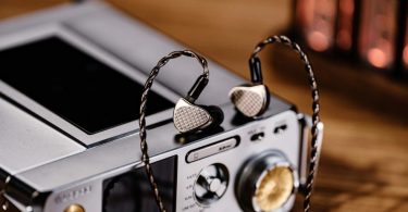 Paire d'IEMs Kiwi Ears Halcyon en finition métal argent avec faceplate à motif répété KE et câble OFC tressé 2-pin, posée sur un DAP audiophile haut de gamme avec sorties multiples 4.4mm, 3.5mm, 6.35mm et XLR4