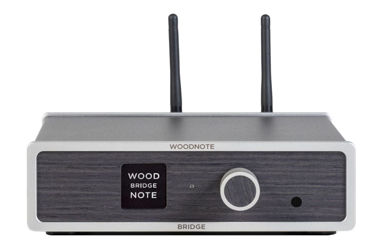 Vue de face frontale du Lindemann Woodnote Bridge avec ses deux antennes télescopiques WLAN et Bluetooth déployées, façade boisée anthracite avec afficheur LCD WOOD BRIDGE NOTE, large bouton de commande rotatif central, marquages WOODNOTE en haut et BRIDGE en bas en lettres argentées