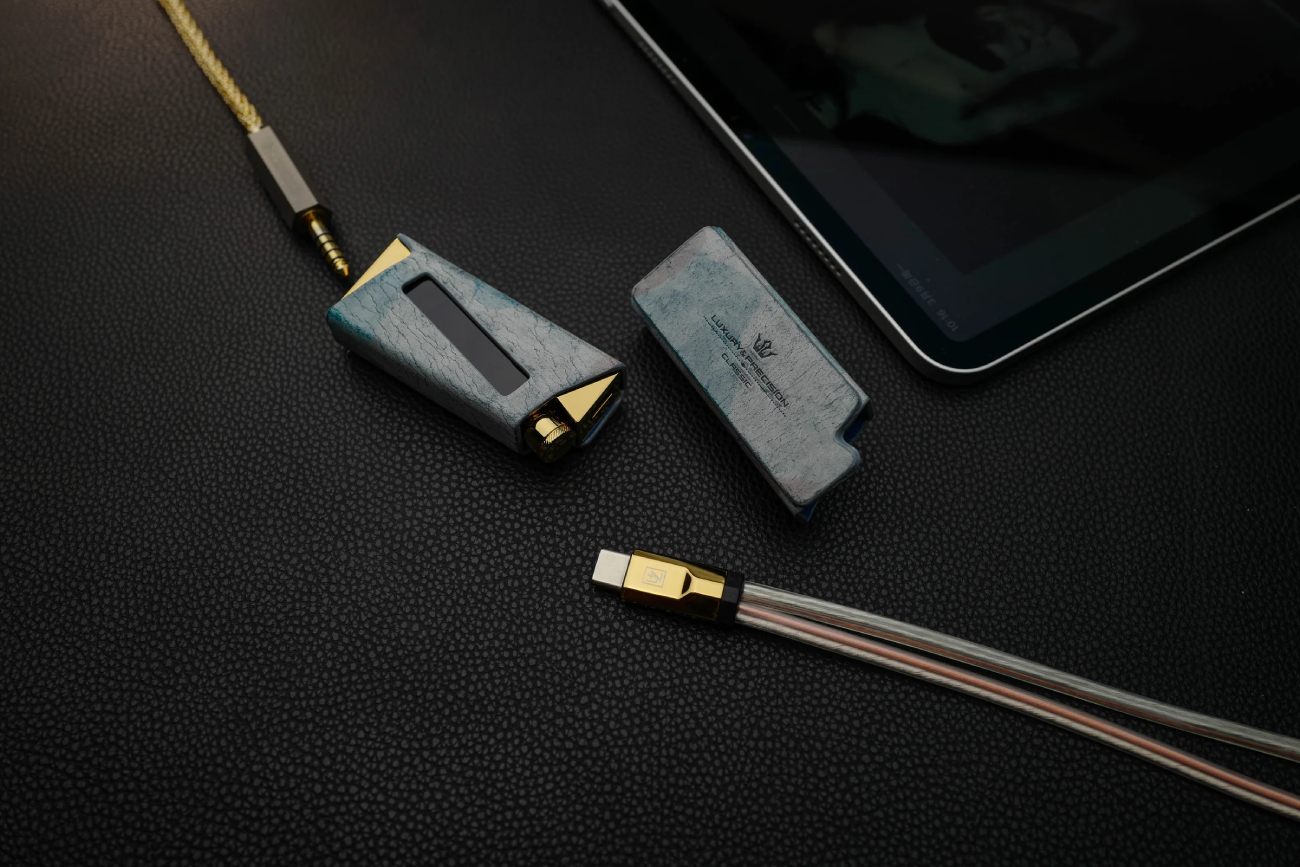 Détail de l'étui en cuir italien tanné végétal du Luxury & Precision W4 ACG Mirror Copper Edition, avec le dongle DAC inséré dans son logement laissant apparaître l'écran OLED et la sortie 4.4 mm balanced occupée par un jack doré tressé, couvercle de protection à droite gravé du logo Luxury & Precision Classic, câble Y WY1 Mirror Copper Special Edition à connecteur USB-C doré visible au premier plan