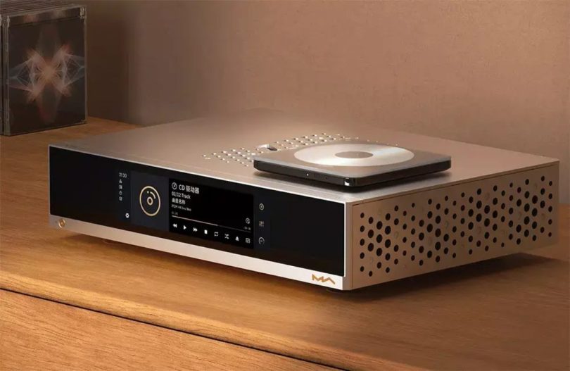 Streamer-DAC Matrix Audio MS-1c en chassis aluminium argent avec écran tactile en façade affichant la lecture d'un CD en PCM 44.1 kHz 16 bit, drive CD USB externe top-loader posé dessus, motif de trous d'aération circulaires sur le côté droit, posé sur table en bois clair