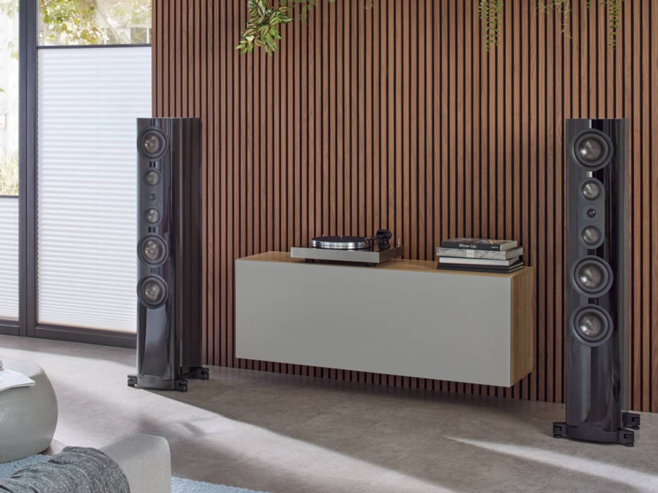 Paire de colonnes passives Nubert nuVero nova en laque piano noire de part et d'autre d'un meuble bas suspendu portant une platine vinyle, dans un salon contemporain à mur en tasseaux de bois, façade galbée et chassis de grave en saillie visibles