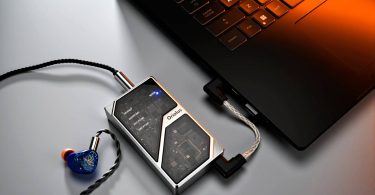 DAC portable Oriolus 1795MKII AL en aluminium avec panneau de verre semi-transparent laissant apparaître le circuit imprimé interne, connecté à un laptop via câble USB-C coudé et à un IEM bleu via sortie 4.4mm balanced à câble tressé argenté