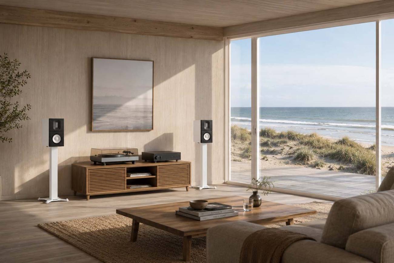 Paire d'enceintes Raidho X1.6 Reference en finition noire sur pieds blancs dans un salon scandinave lumineux face à la mer, associées à une platine vinyle et un amplificateur posés sur un meuble bas en bois clair