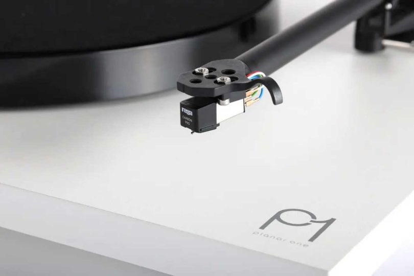 Gros plan macro sur le diamant elliptique Rega Carbon Pro monté sur la cellule MM Carbon noire d'une platine vinyle Rega Planar 1 finition blanche, cantilever et fils de cellule visibles, bras de lecture RB110 en arrière-plan