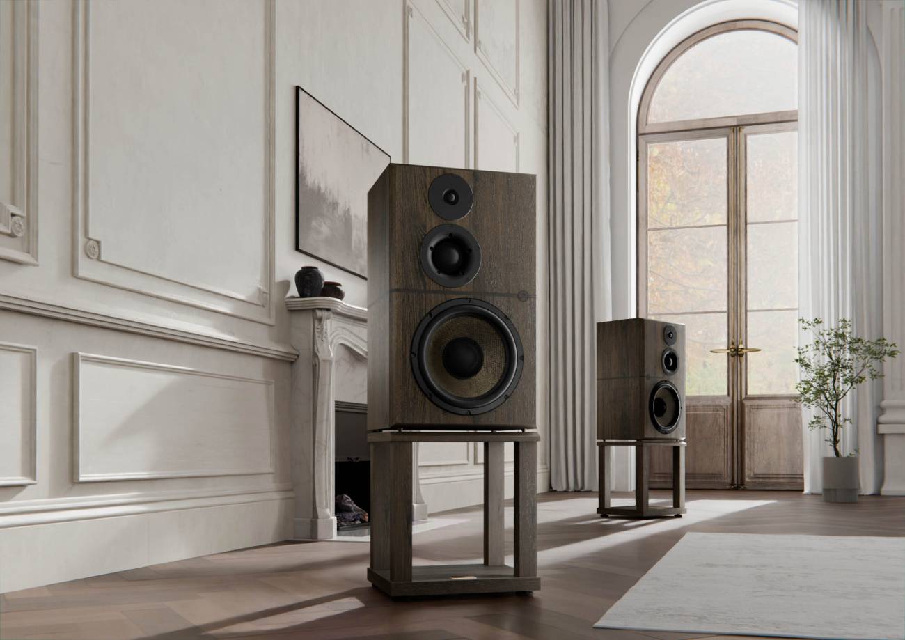 Détail de la Revival Audio Atalante Grande Réserve en finition chêne fumé sur son stand dédié, premier plan sur la face avant montrant le tweeter 28 mm RASC Évo en partie haute, le médium 75 mm RASC Évo à dôme souple au centre, et le woofer 12 pouces BSC Grande Réserve avec son cône en construction sandwich basalte couleur cuivre métallisé et son cache-noyau noir, dans un salon classique avec porte-fenêtre arquée et parquet en chevrons