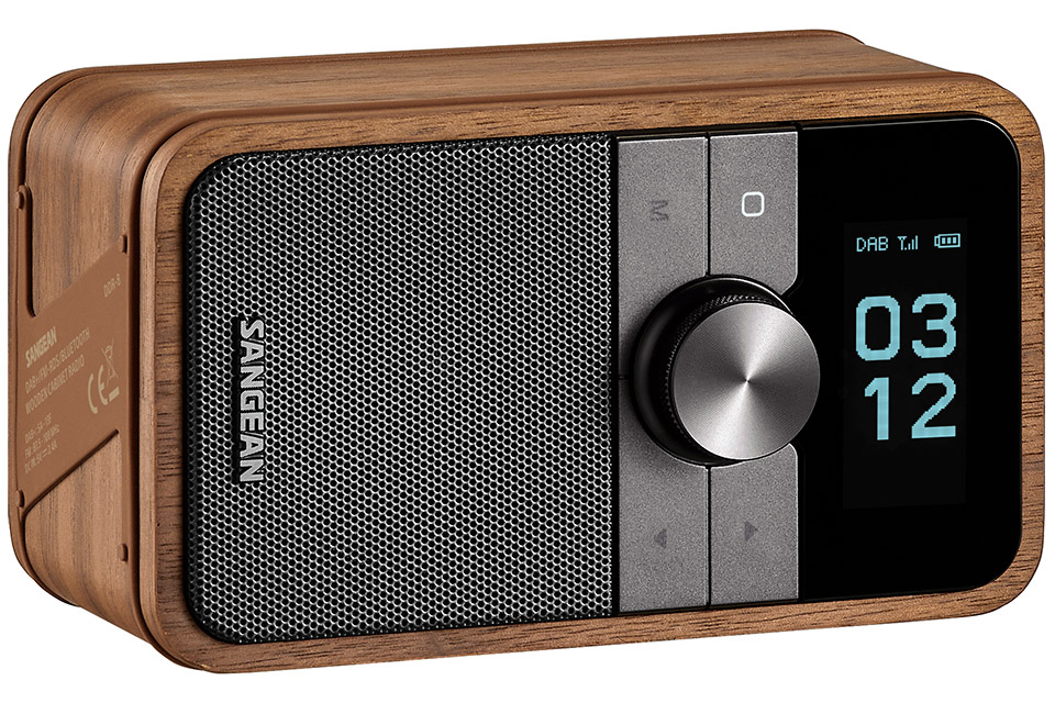 Sangean DDR-8 radio portable DAB+ FM-RDS Bluetooth 5.2 en finition Vintage Walnut, vue produit trois quarts en orientation horizontale, détail du bouton rotatif central en métal brossé, écran OLED affichant l'heure 03:12 en mode flip-clock avec indicateurs DAB signal et batterie, grille tissée gris argent du haut-parleur 2 pouces avec logo SANGEAN, étiquette technique latérale visible