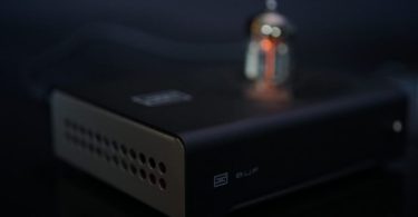 Tube buffer Schiit Buf en chassis noir mat avec côté champagne perforé, logo Schiit et marquage BUF, tube 6N1P rougeoyant visible à l'arrière en bokeh, ambiance studio audiophile sombre