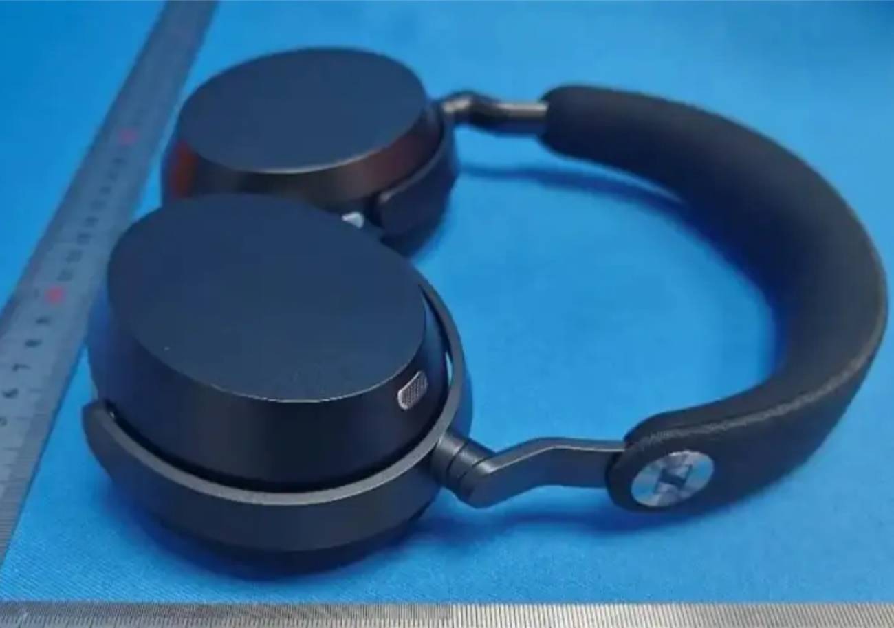 Photo leak du Sennheiser Momentum 5 Wireless issue d'une base de certification réglementaire (FCC, MIC ou RRA), casque noir sans-fil posé sur fond bleu de labo avec règle métallique d'échelle, ear cups circulaires plats, arceau tissu noir, yoke métallique articulé et logo S Sennheiser visible