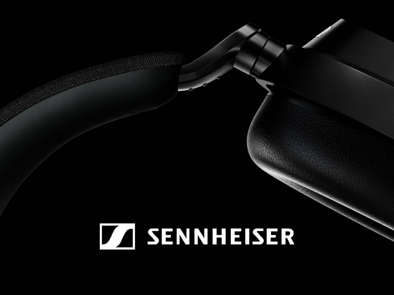 Gros plan macro officiel du nouveau casque sans-fil Sennheiser teaser, détail du yoke métallique articulé en noir mat, arceau habillé de tissu noir avec rembourrage, oreillette avec coussinet en simili-cuir noir grainé, fond noir et logo SENNHEISER