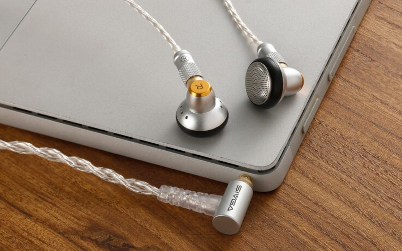 Mise en scène des Sivga M260 version 3,5 mm posés sur un ordinateur portable en aluminium argenté sur un bureau en bois noyer. Vue détaillée de la fiche jack 3,5 mm L-shaped en aluminium brossé avec logo Sivga gravé et bague laiton, du connecteur MMCX moleté avec marquage R doré, du grillage frontal en façade du driver dynamique 14,2 mm visible sur l'écouteur droit, et du câble argenté 4N OFC tressé plaqué argent