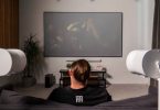Configuration home cinéma Sonos en situation : barre de son Arc Ultra et caisson Sub 4 sous un grand téléviseur, encadrés par deux enceintes Era 300 blanches montées sur pieds en position surround, dans un salon contemporain pour une écoute Dolby Atmos