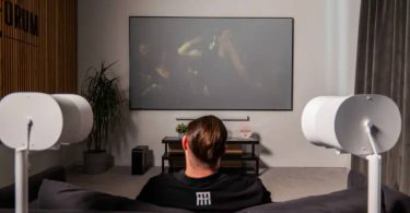 Configuration home cinéma Sonos en situation : barre de son Arc Ultra et caisson Sub 4 sous un grand téléviseur, encadrés par deux enceintes Era 300 blanches montées sur pieds en position surround, dans un salon contemporain pour une écoute Dolby Atmos
