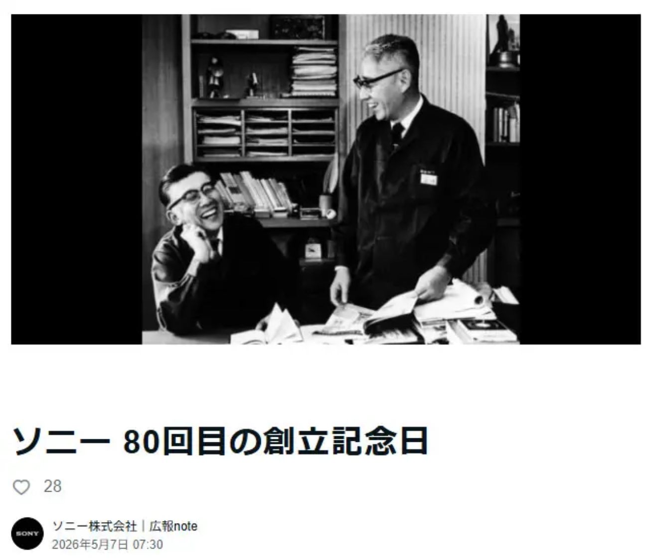 Photo officielle d'archive Sony Corporation publiée pour le 80e anniversaire en 2026 montrant Akio Morita assis à gauche en costume sombre la main contre la joue éclatant de rire et Masaru Ibuka debout à droite en blouse de travail avec lunettes consultant des documents techniques sur un bureau encombré de livres et magazines, dans le siège historique de Tokyo Tsushin Kogyo