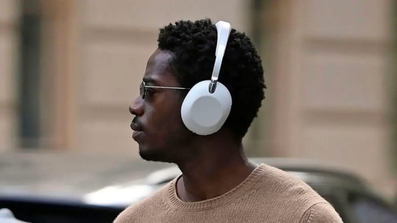 Sony WH-1000XX 1000X The ColleXion casque sans-fil à réduction de bruit active édition limitée 10e anniversaire de la gamme 1000X 2026 vue de profil porté en situation extérieure rue de New York coloris blanc avec éléments métalliques argentés bandeau métallique fin et minimaliste arceau métal articulation charnière métal apparente entre arceau et pavillon, pavillon arrondi à finition mate avec garniture en cuir synthétique premium, nouvelle articulation où les bras s'enfoncent dans le pavillon vs assemblage par-dessus sur WH-1000XM6, contour en métal autour de la prise jack 3.5mm, casque aperçu in the wild à la suite d'une fuite produit avant lancement officiel le 19 mai 2026 au tarif de 629 euros en Europe