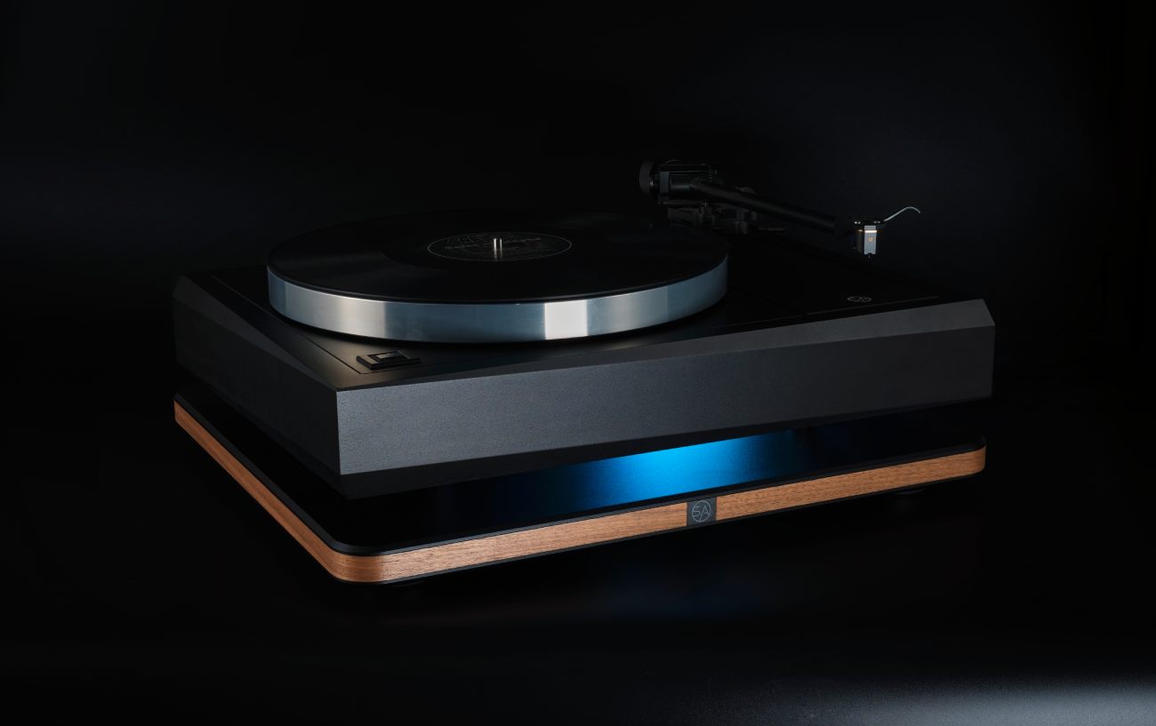 Plateforme d'isolation vibratoire Stack Audio AUVA Platform en finition placage noyer avec plaque centrale aluminium noir anodisé, logo SA visible en façade, supportant une platine vinyle Linn Sondek LP12 Serene noire, rétroéclairage bleu illustrant le découplage mécanique entre les deux étages de la plateforme