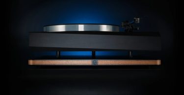 Plateforme d'isolation vibratoire Stack Audio AUVA Platform en situation sous une platine vinyle haut de gamme à ébénisterie loupe, avec rétroéclairage bleu illustrant la séparation mécanique entre les deux plaques aluminium anodisé qui encadrent la structure honeycomb à 35 cellules de particle damping