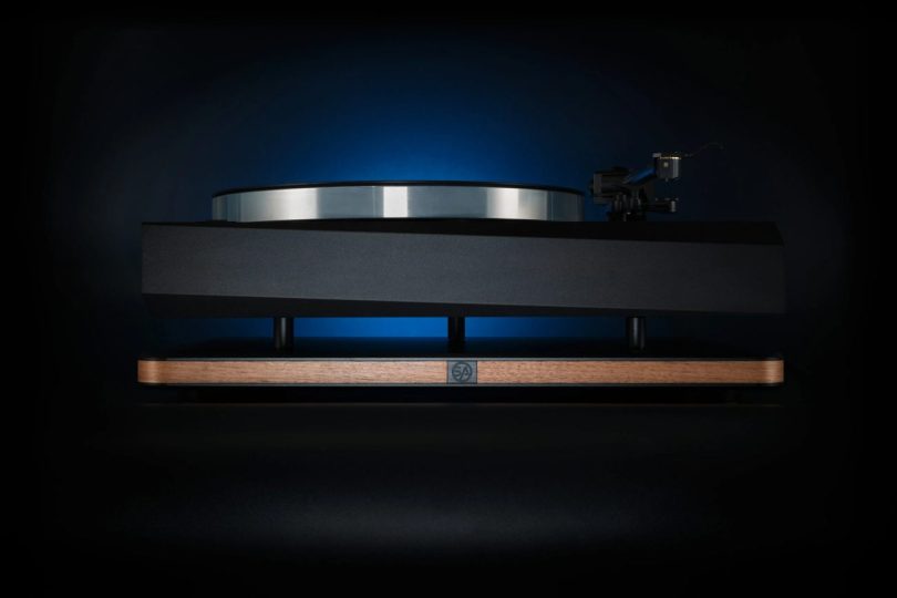 Plateforme d'isolation vibratoire Stack Audio AUVA Platform en situation sous une platine vinyle haut de gamme à ébénisterie loupe, avec rétroéclairage bleu illustrant la séparation mécanique entre les deux plaques aluminium anodisé qui encadrent la structure honeycomb à 35 cellules de particle damping