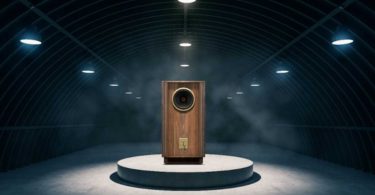 Enceinte Tannoy Prestige Gold Reference édition anniversaire 100 ans en finition noyer huilé, mise en scène dans un loft industriel avec briques rouges et grandes baies vitrées, haut-parleur Dual Concentric 15 pouces visible derrière le pavillon avant.