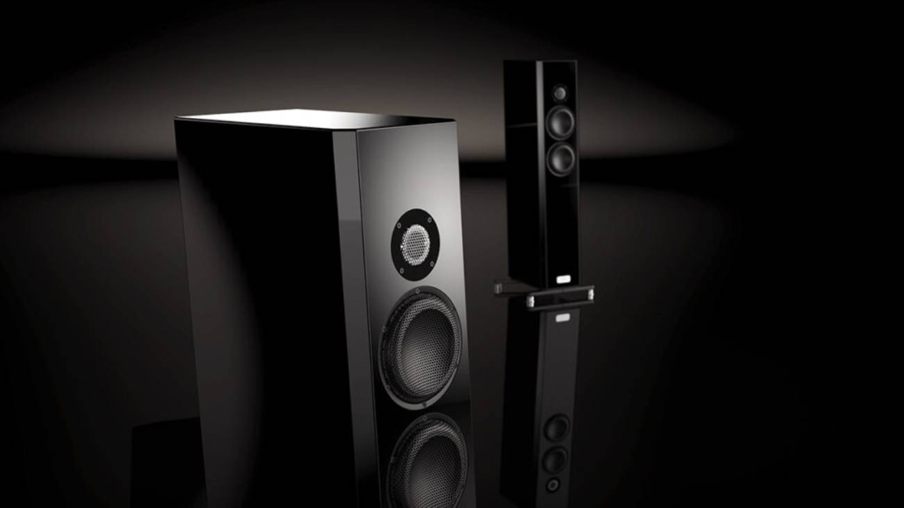 Détail rapproché des transducteurs TIDAL Piano Classic en finition laque piano Midnight Black : tweeter dôme céramique noire 30 mm avec grille protectrice et mid-woofer crystalid 170 mm avec grille ronde. Seconde enceinte visible en arrière-plan sur fond noir gradient et sol miroir.