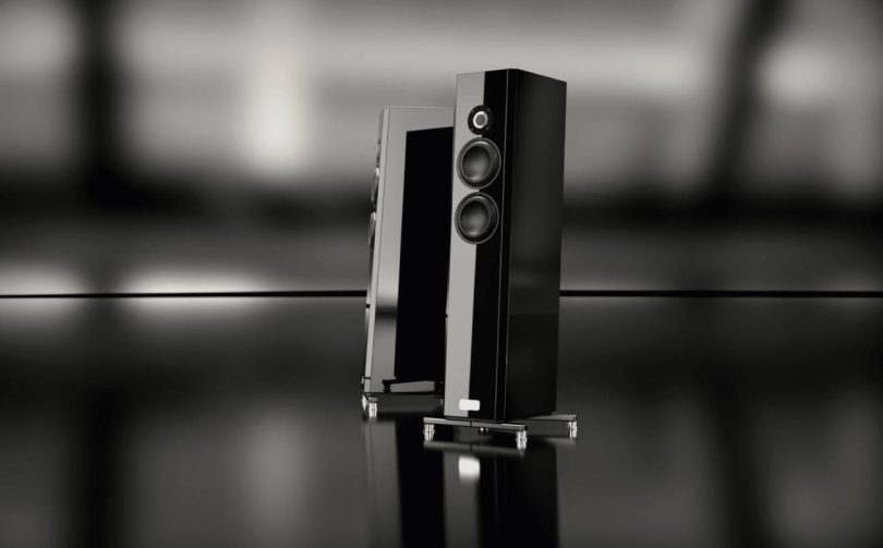 Paire d'enceintes colonne TIDAL Piano Classic en finition laque piano Midnight Black, vues de trois quarts sur sol miroir noir. Tweeter céramique noire 1,2 pouce et deux mid-woofers crystalid 7 pouces visibles en façade, embase acier inoxydable et isolators apparents.