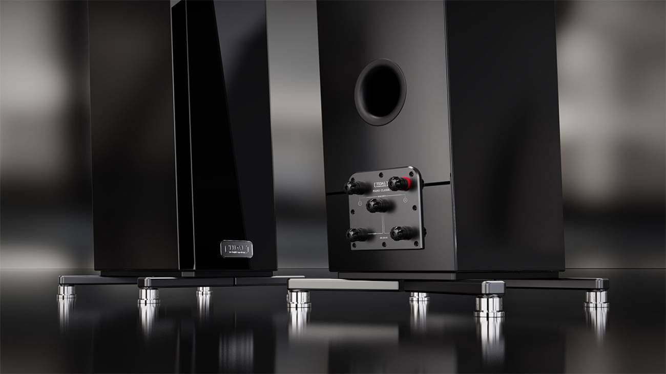 Vue arrière de la TIDAL Piano Classic en finition laque piano Midnight Black montrant le terminal Vario à quatre bornes silver binding posts avec marquage TIDAL Piano Classic, l'évent bass-reflex circulaire en partie haute, et l'embase en acier inoxydable avec ses isolators polis. Seconde enceinte vue de profil arrière à gauche avec son badge TIDAL argenté incrusté.Vue arrière de la TIDAL Piano Classic en finition laque piano Midnight Black montrant le terminal Vario à quatre bornes silver binding posts avec marquage TIDAL Piano Classic, l'évent bass-reflex circulaire en partie haute, et l'embase en acier inoxydable avec ses isolators polis. Seconde enceinte vue de profil arrière à gauche avec son badge TIDAL argenté incrusté.