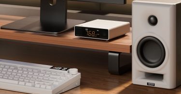 TOPPING E50II en finition argent posé sur une étagère en bois clair sous un écran d'ordinateur, écran orange affichant USB BAL 768.0 PCM, avec à droite une enceinte de monitoring TOPPING Professional et au premier plan un clavier mécanique blanc