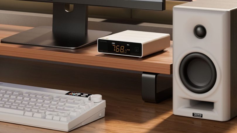 TOPPING E50II en finition argent posé sur une étagère en bois clair sous un écran d'ordinateur, écran orange affichant USB BAL 768.0 PCM, avec à droite une enceinte de monitoring TOPPING Professional et au premier plan un clavier mécanique blanc