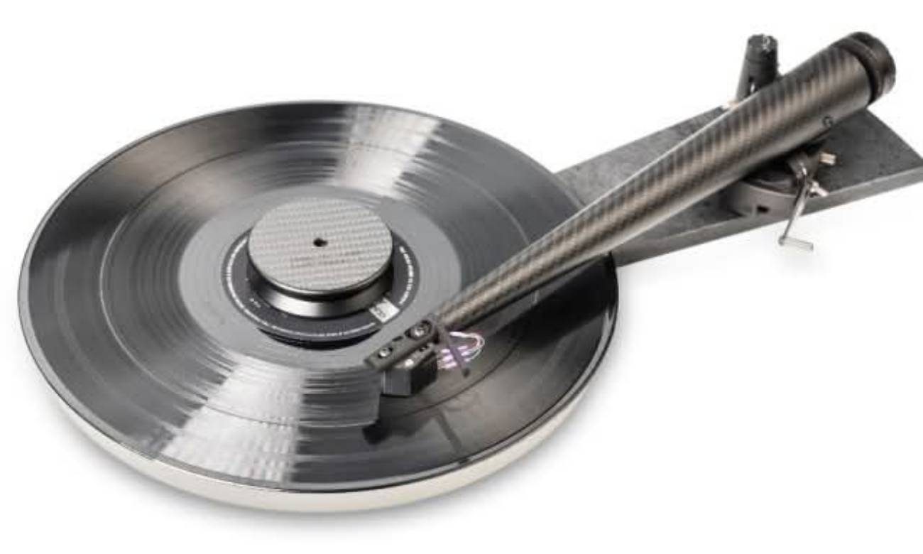 Vue d'ensemble en plongée du système Wand complet : plateau de platine massif en aluminium avec disque microsillon en lecture, centre presseur Wand Weight à finition texturée carbone posé au centre, bras de lecture Dark-Light 12 pouces en fibre de carbone tressée à profil Musical Taper monté sur sa base avec pivot ZeroPoint et bras de relevage manuel visible