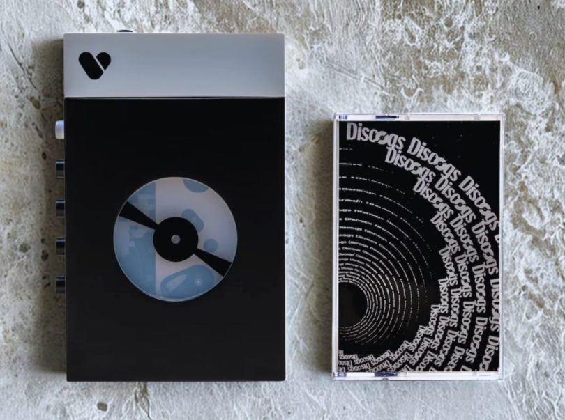 Lecteur cassette portable We Are Rewind WE-001 Discogs Edition en finition Matte Black exclusive avec logo Discogs sur la fenêtre de visualisation cassette, châssis en alliage d'aluminium compact, contrôles de lecture et fenêtre transparente laissant voir la cassette en cours, vue de trois-quarts sur fond neutre