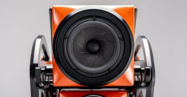 Vue rapprochée d'un driver médium 7 pouces PentaMag de l'enceinte flagship Wilson Audio Autobiography en finition Red Rock Sunset orange, montrant le cône en composite, le cache anti-poussière, le bague de fixation noir mat et les supports d'alignement en aluminium machiné noir avec leur cam d'ajustement temporel mécanique