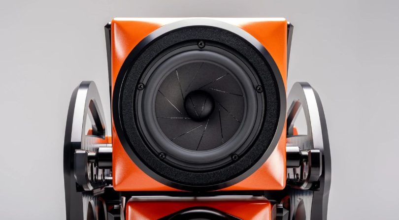 Vue rapprochée d'un driver médium 7 pouces PentaMag de l'enceinte flagship Wilson Audio Autobiography en finition Red Rock Sunset orange, montrant le cône en composite, le cache anti-poussière, le bague de fixation noir mat et les supports d'alignement en aluminium machiné noir avec leur cam d'ajustement temporel mécanique