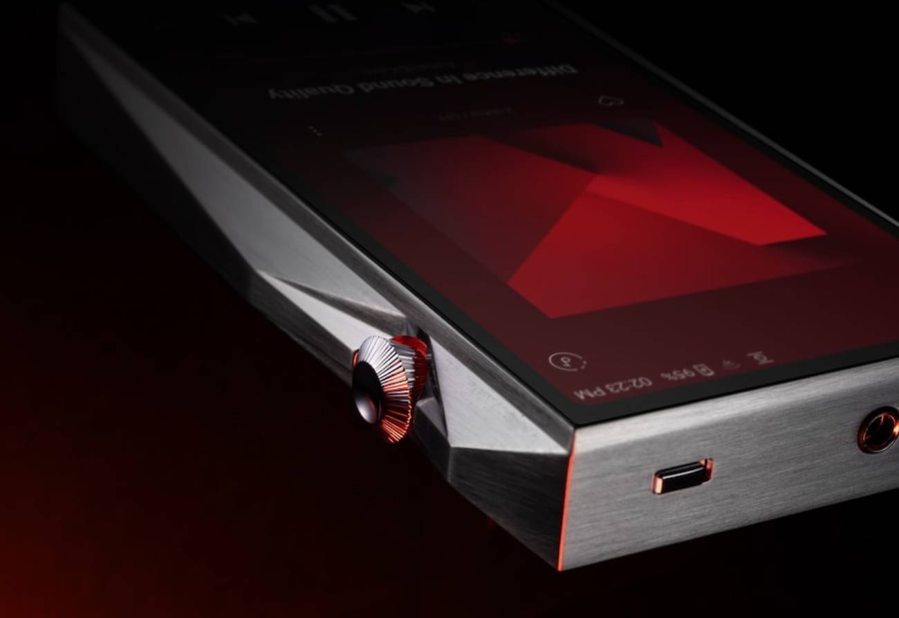 Détail en angle du baladeur Astell&Kern SP4000T en acier inox brossé montrant la molette de volume crantée à liseré rouge, le châssis taillé en facettes, le port USB-C et la sortie casque sur la tranche