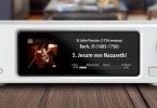 Aurender DA100, streaming DAC dual-mono AK4499 en finition blanche posé sur un plan en bois, écran IPS affichant une lecture TIDAL haute résolution, bouton de veille rétroéclairé bleu à gauche et molette de volume à droite