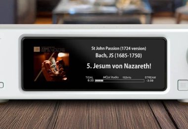 Aurender DA100, streaming DAC dual-mono AK4499 en finition blanche posé sur un plan en bois, écran IPS affichant une lecture TIDAL haute résolution, bouton de veille rétroéclairé bleu à gauche et molette de volume à droite