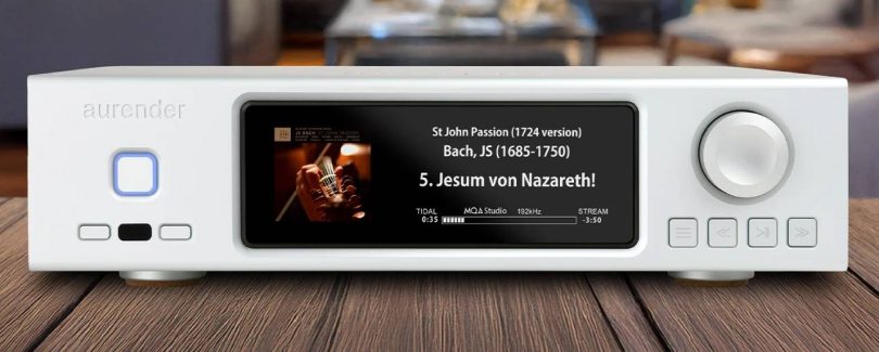 Aurender DA100, streaming DAC dual-mono AK4499 en finition blanche posé sur un plan en bois, écran IPS affichant une lecture TIDAL haute résolution, bouton de veille rétroéclairé bleu à gauche et molette de volume à droite