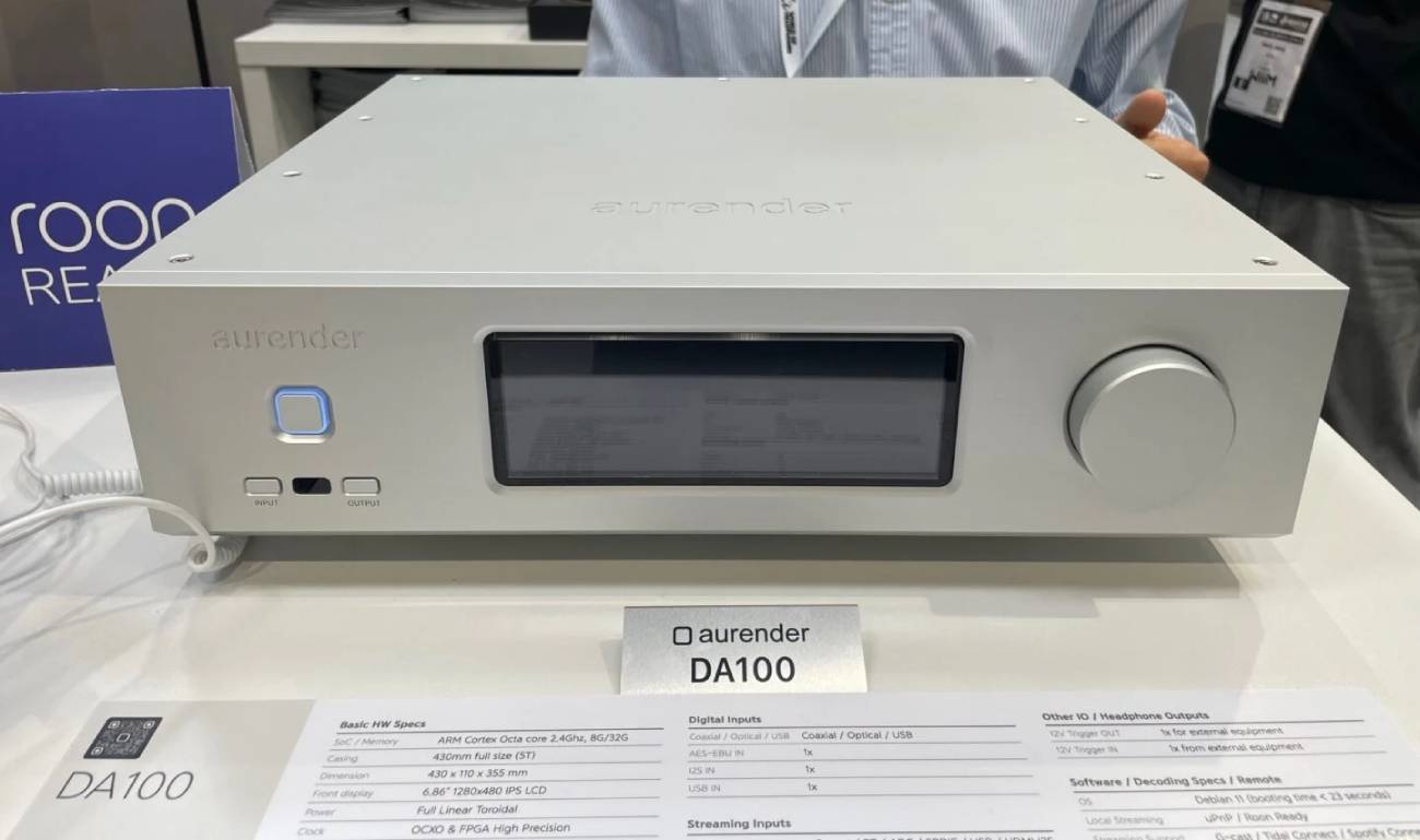Aurender DA100 vu de face en finition argent, large écran IPS 6,86 pouces, bouton de veille rétroéclairé bleu, touches INPUT et OUTPUT et molette de volume, exposé à Vienna High End 2026