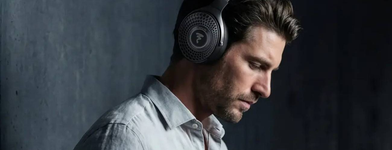Homme portant le casque Bluetooth Focal Bathys MG en finition Graphen Grey gris minéral, logo Focal sur la grille perforée de l'oreillette et inscription FOCAL sur l'arceau, ambiance feutrée sur fond de mur béton sombre
