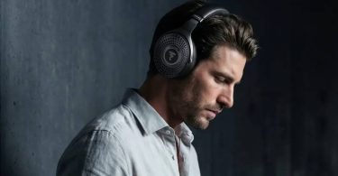 Homme portant le casque Bluetooth Focal Bathys MG en finition Graphen Grey gris minéral, logo Focal sur la grille perforée de l'oreillette et inscription FOCAL sur l'arceau, ambiance feutrée sur fond de mur béton sombre