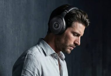 Homme portant le casque Bluetooth Focal Bathys MG en finition Graphen Grey gris minéral, logo Focal sur la grille perforée de l'oreillette et inscription FOCAL sur l'arceau, ambiance feutrée sur fond de mur béton sombre