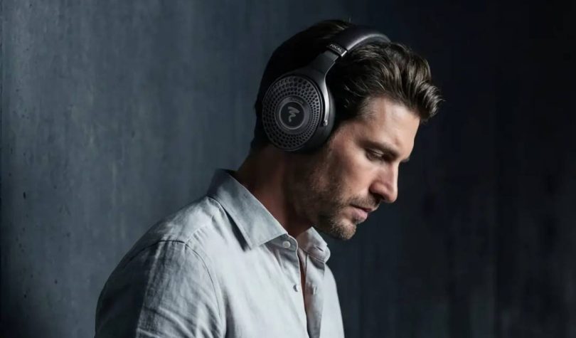 Homme portant le casque Bluetooth Focal Bathys MG en finition Graphen Grey gris minéral, logo Focal sur la grille perforée de l'oreillette et inscription FOCAL sur l'arceau, ambiance feutrée sur fond de mur béton sombre