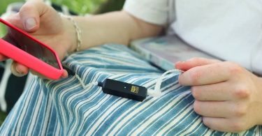 Dongle DAC USB-C iFi GO link 2 Max noir avec logo Hi-Res Audio doré et LED allumée, posé sur les genoux, relié d'un côté à un smartphone en coque rouge et de l'autre à des IEM par un câble argenté, en écoute nomade en extérieur
