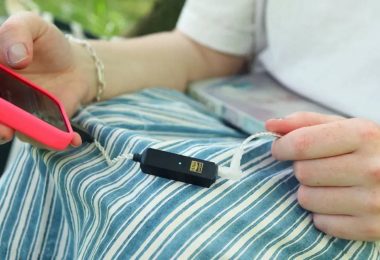 Dongle DAC USB-C iFi GO link 2 Max noir avec logo Hi-Res Audio doré et LED allumée, posé sur les genoux, relié d'un côté à un smartphone en coque rouge et de l'autre à des IEM par un câble argenté, en écoute nomade en extérieur