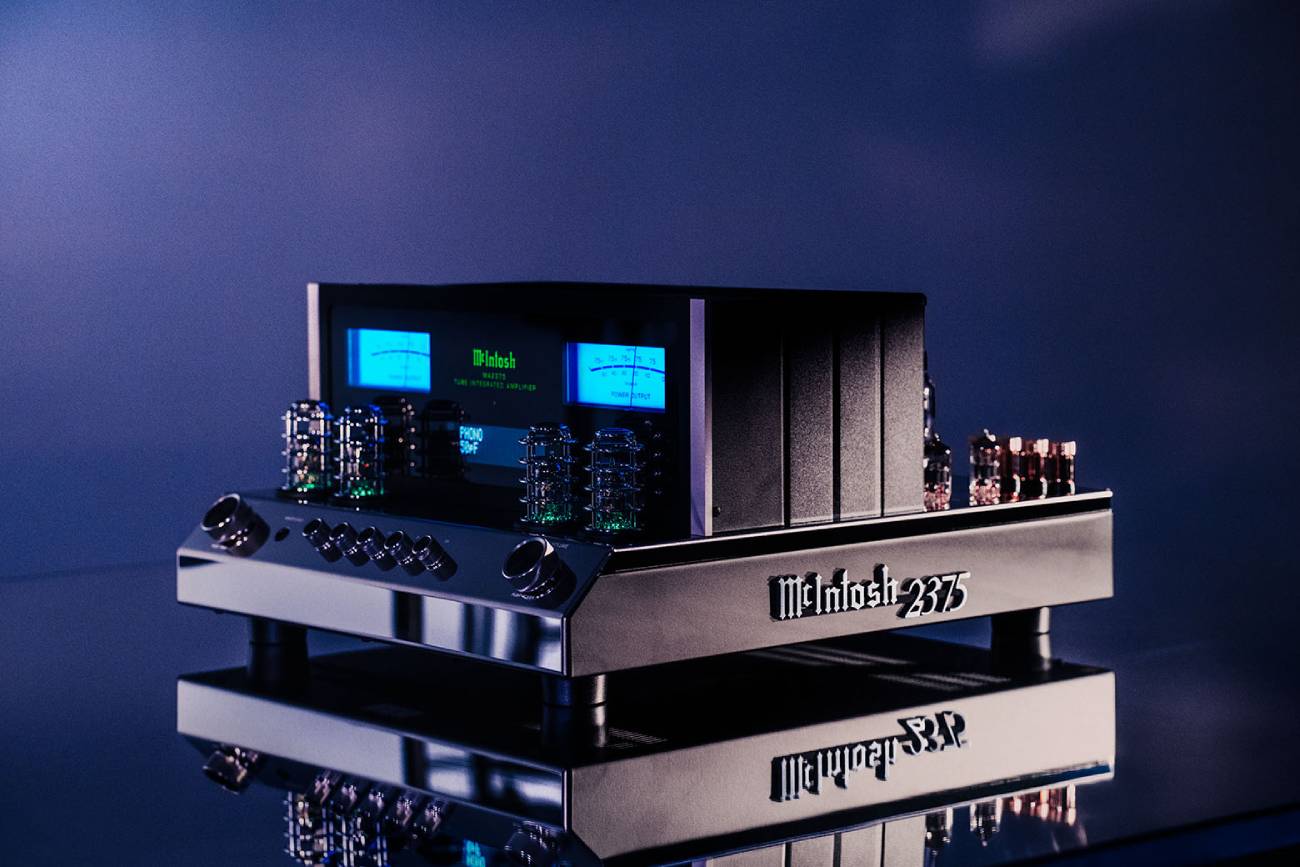 Amplificateur intégré à tubes McIntosh MA2375 vu de trois quarts sur fond bleu, châssis inox poli avec badge gothique McIntosh 2375, vumètres bleus rétroéclairés, tubes apparents sous leurs cages de protection et radiateurs latéraux